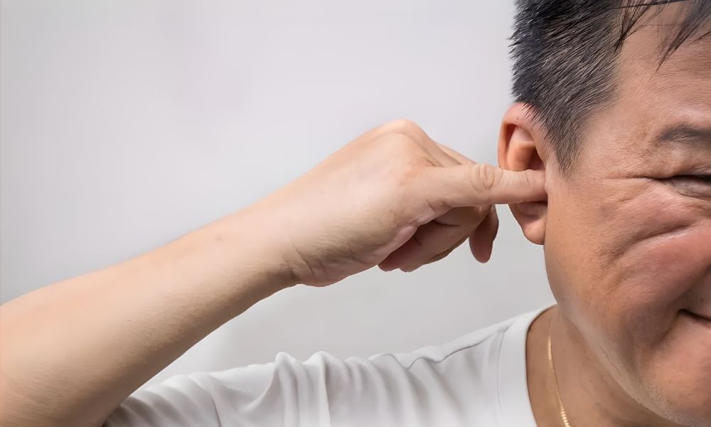 Man putting a finger in his ear, a common cause of ear wax build-up in Belfast.